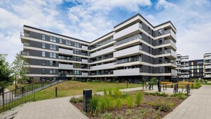 Un moderno edificio residencial de varios pisos con balcones, un patio ajardinado y un sendero pavimentado.