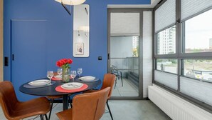 A dining area with a blue wall, a round table set for four, and a view of the city through large windows. - Modern Apartment with Balcony | Parking, Close to the River (Gdansk)