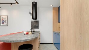 A modern kitchen with a curved island, bar stools, a black hanging light fixture, and a wooden cabinet. - Modern Apartment with Balcony | Parking, Close to the River (Gdansk)