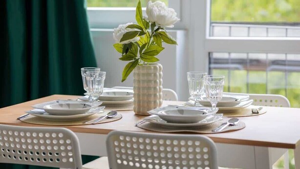 A dining table set with plates, glasses, and cutlery, with a vase of flowers in the center. - Apartment with 2 Bedrooms in Wola | Workspace (Warszawa)