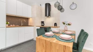 Eine moderne Küche mit weißen Schränken, einem Holztisch, der mit rosa Tellern und grünen Platzsets gedeckt ist, und einem mit grünem Stoff gepolsterten Stuhl.