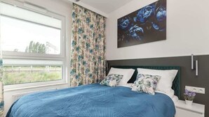 Ein Schlafzimmer mit einem großen Bett, floralen Vorhängen, einem Gemälde und Blick ins Freie.