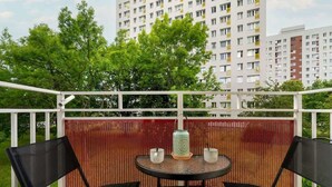 A balcony with a table and chairs, a decorative lantern, and a view of a multi-story building with balconies. - Traditional Apartment with Balcony | Close to the Park (Poznan)