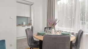 A modern dining area with a round table, grey upholstered chairs, and a vase with flowers. - Traditional Apartment with Balcony | Close to the Park (Poznan)