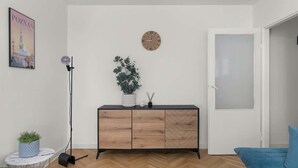 A modern living room with a herringbone wood floor, a black sofa, a white door, a wooden cabinet with a clock, and a framed picture on the wall. - Traditional Apartment with Balcony | Close to the Park (Poznan)