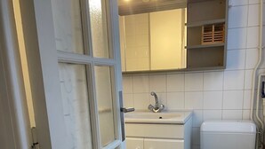 Une salle de bain avec des toilettes blanches, un lavabo et un miroir au-dessus. On y trouve un porte-serviettes avec des serviettes pliées.