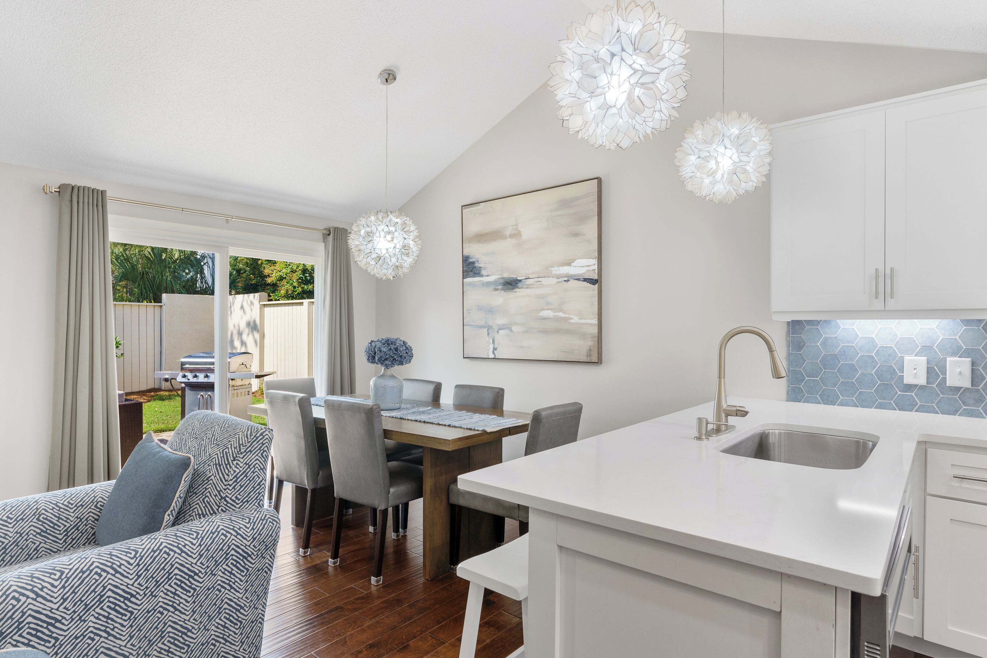 A modern kitchen with white cabinetry, a large island with a sink, and a dining area with a table and chairs.