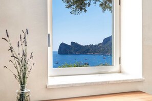 A room with a large window overlooking a coastal view with boats and rocky cliffs.