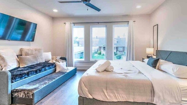 Ein modernes Schlafzimmer mit einem Bett, einer Couch, einem Deckenventilator und einem an der Wand montierten Fernseher.