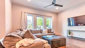 Ein modernes Wohnzimmer mit einem Ecksofa, einem Hocker und einem an der Wand befestigten Flachbildfernseher.