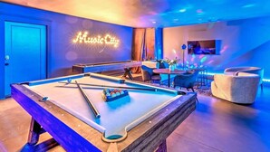 Une table de billard avec un panneau néon indiquant « Music City », dans une pièce éclairée d’une lumière ambiante bleue et dotée de meubles modernes.
