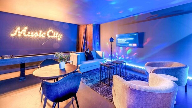 Un espace de détente moderne avec un panneau néon indiquant « Music City », un téléviseur, des sièges confortables et une piste de bowling.