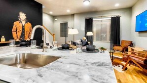 A modern kitchen with a marble countertop, stainless steel sink, and a dining area with wooden chairs and a table.