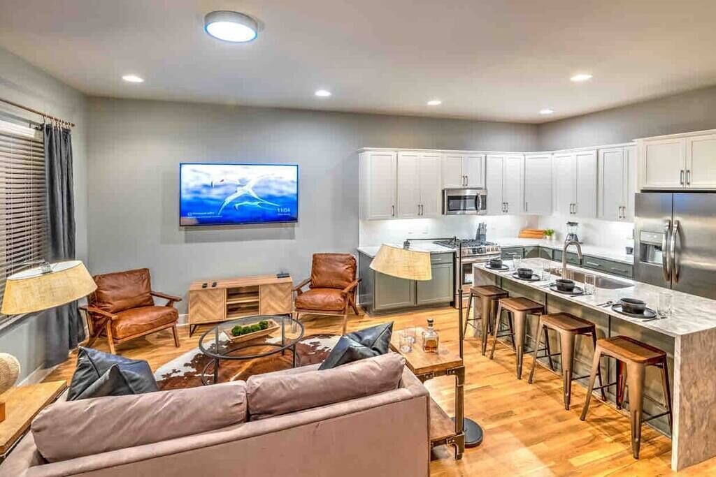 A modern kitchen with white cabinets, a stainless steel refrigerator, and a bar area with stools.