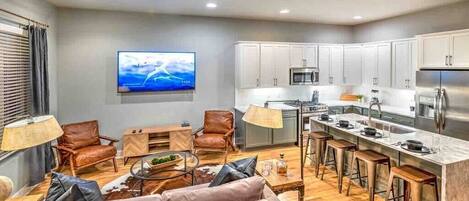 A modern kitchen with white cabinets, a stainless steel refrigerator, and a bar area with stools.