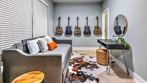 A hallway with a grey sofa, a round wooden side table, a mirror, and a wall with six guitars.