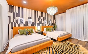 A hotel room with two beds, a zebra-patterned rug, a chandelier, and a striped wall design.