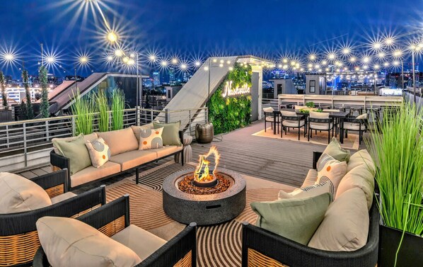 Eine Dachterrasse mit Feuerstelle, Sitzbereich und Blick auf die Stadtlandschaft.