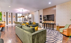 A modern living room with a sofa, chairs, a TV, and a kitchen in the background.