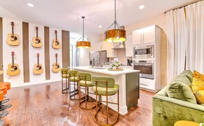 A modern kitchen with a central island, bar stools, and a green sofa.