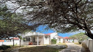 A paved pathway leading to a building with a red roof, surrounded by trees and a fenced area. - Newly updated 3BD 2BA House, close to Palm Beach, shops and dining (Noord)