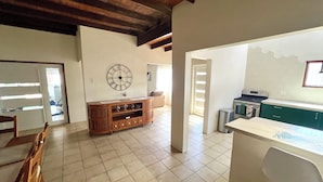 A spacious living area with a wooden entertainment unit, a large wall clock, and a kitchen area with green cabinets and a white countertop. - Newly updated 3BD 2BA House, close to Palm Beach, shops and dining (Noord)