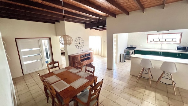 A spacious dining area with a wooden table and chairs, a kitchen with a green countertop, and a tiled floor. - Newly updated 3BD 2BA House, close to Palm Beach, shops and dining (Noord)