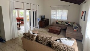 A living room with a sofa, a television, and a fan. There are curtains and a window. - Newly updated 3BD 2BA House, close to Palm Beach, shops and dining (Noord)
