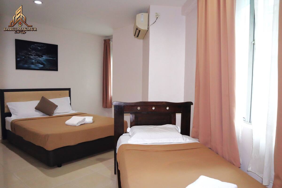 Une chambre d’hôtel avec deux lits, une literie de couleur beige, une affiche représentant un ciel étoilé, une fenêtre avec des rideaux et un climatiseur fixé au mur.
