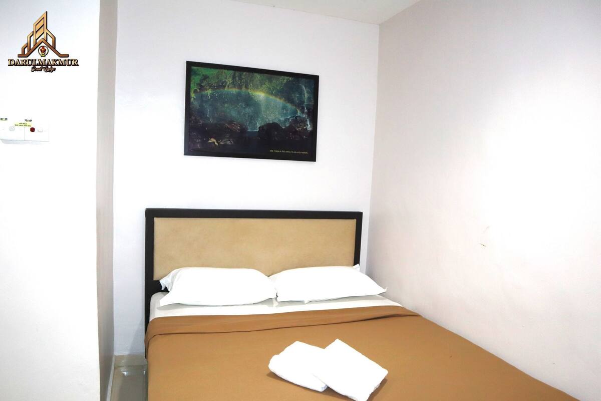 Une chambre d’hôtel avec un lit, des oreillers blancs, une couverture marron et un tableau représentant un paysage naturel accroché au mur.