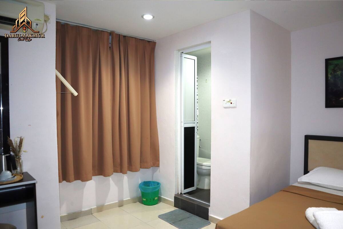 Une chambre d’hôtel avec un lit, un bureau, une salle de bain visible à travers une porte ouverte et un rideau à la fenêtre.