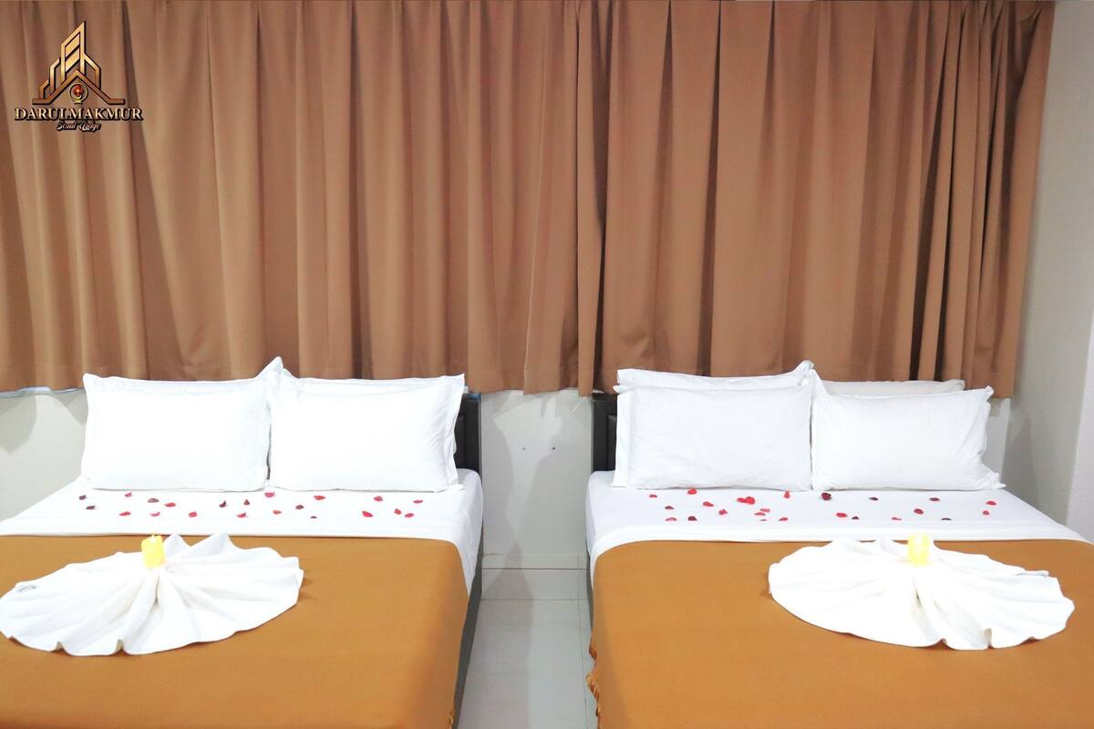 Deux lits avec des draps blancs et des couvre-lits marron, chacun agrémenté d’une serviette blanche et de pétales de rose.