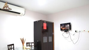 Egy szoba, melyben üveglapú asztal, két szék, egy fekete szekrény, a falra szerelt televízió és egy légkondicionáló található.