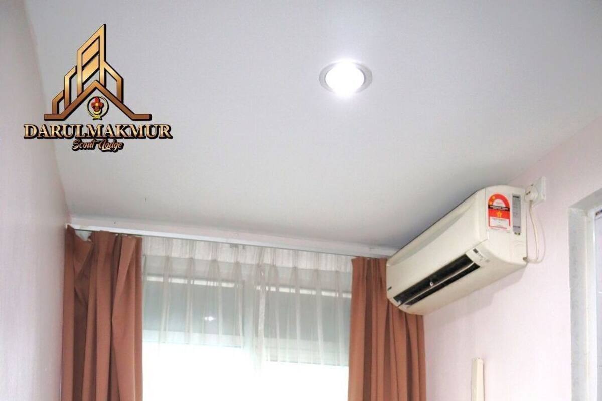 Une chambre d’hôtel avec un lit, des rideaux marron, un appareil de climatisation et une fenêtre avec des rideaux légers.