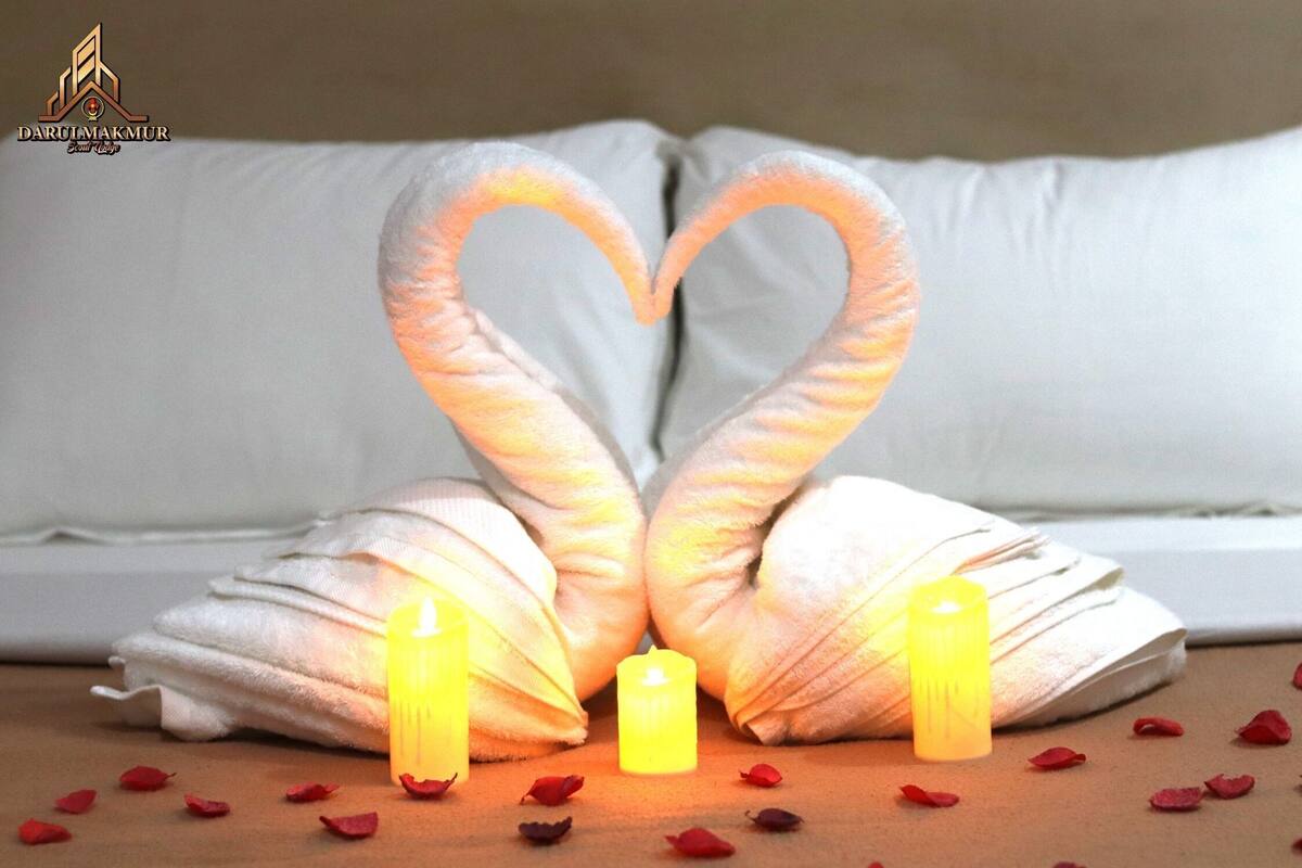 Une serviette pliée en forme de cœur, agrémentée de bougies et de pétales de rose, posée sur une surface en bois.