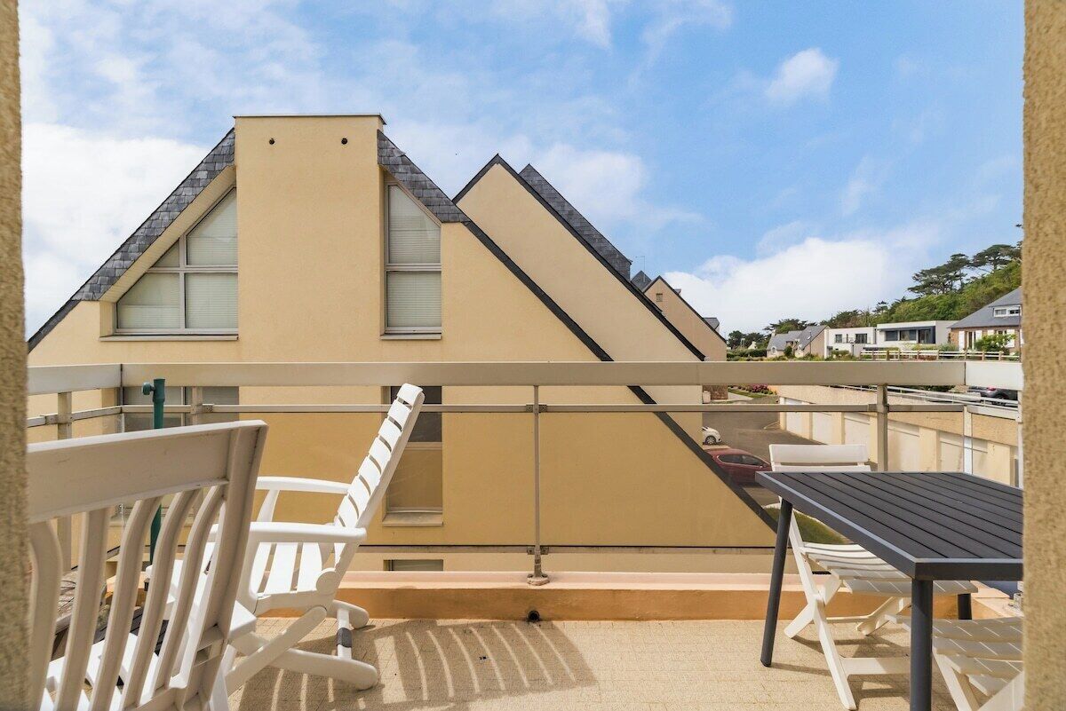 A balcony with a table and chairs, overlooking a residential area with houses.