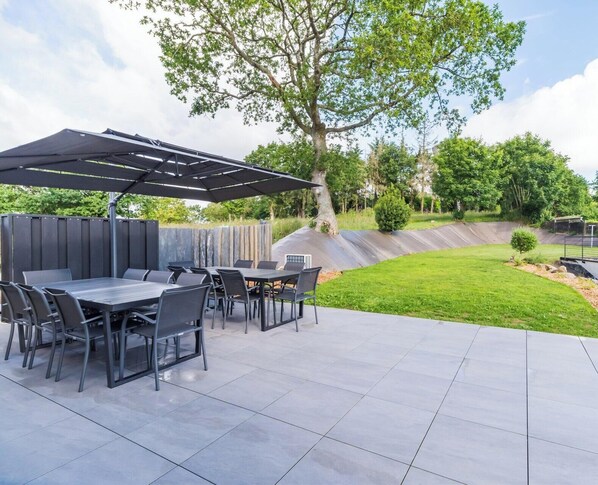 An outdoor patio with a table and chairs, a covered area, and a landscaped garden. - Large house: billiards, garden, beaches 25 min (Saint-Carreuc)