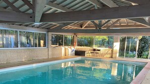Piscina interior con agua azul cristalina, rodeada de baldosas de piedra y cubierta de madera.