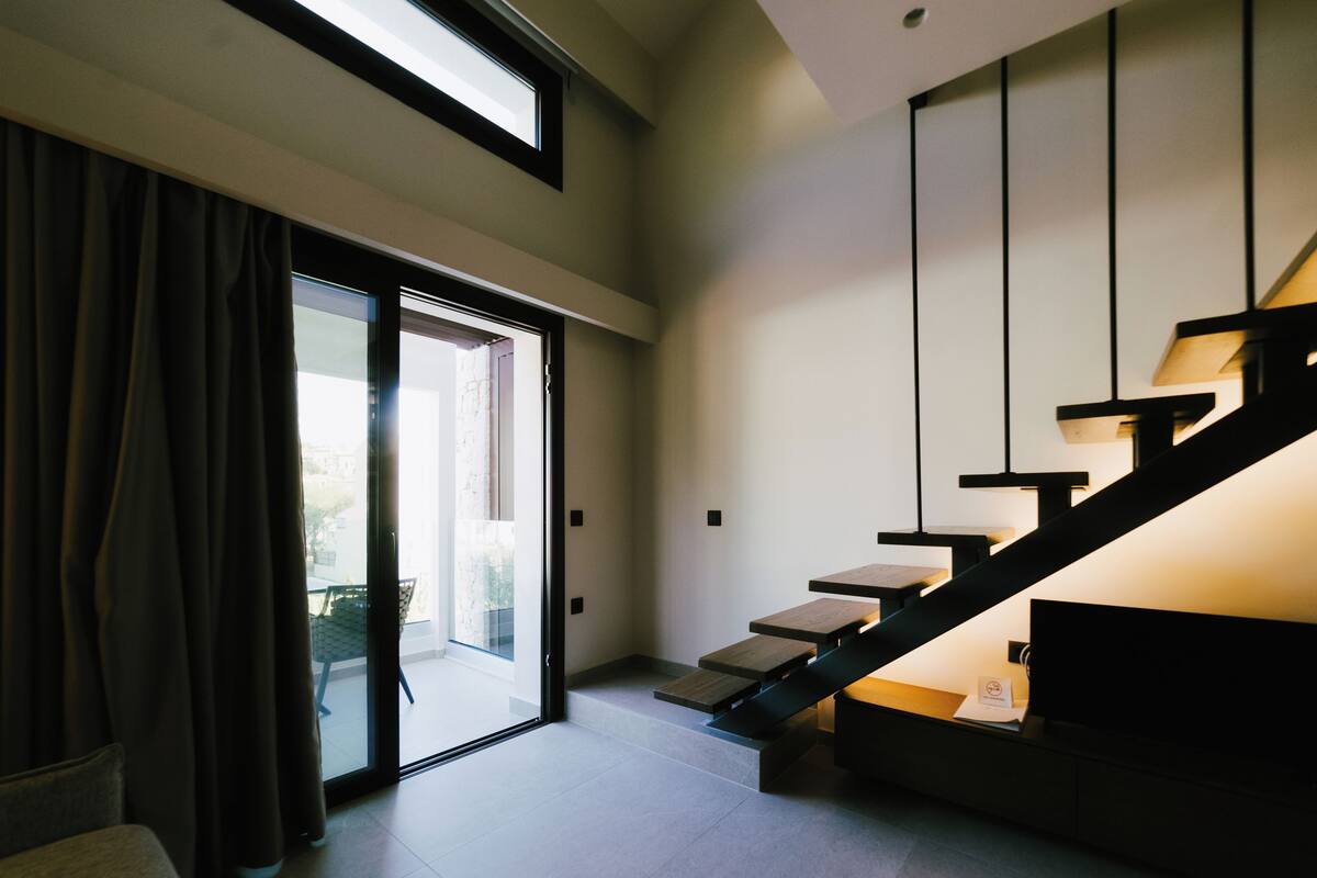 A modern interior with a staircase, a sliding glass door leading to a balcony, and a minimalist design.