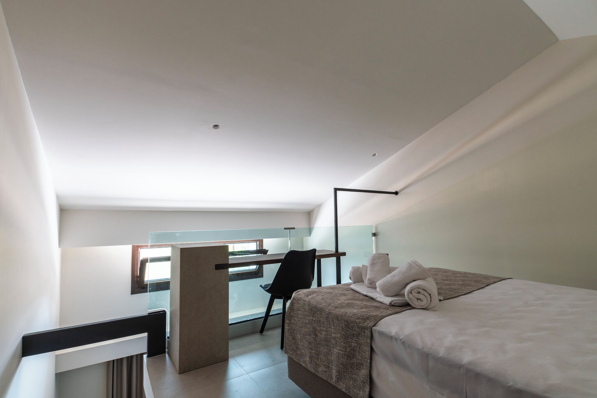 A modern hotel room with a bed, a desk, and a chair.