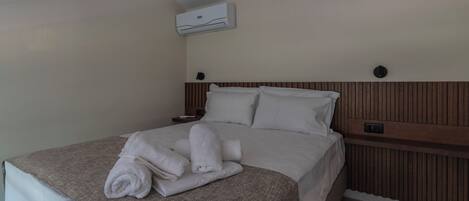 A neatly made bed with a brown blanket and rolled towels, a wooden headboard, and an air conditioning unit on the wall.