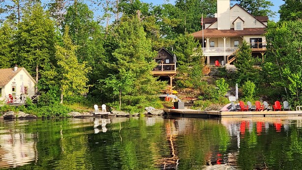 A lakeside property with a dock, a wooden house, and a larger house with a balcony.