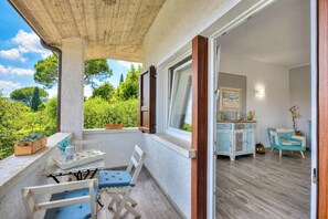 A balcony with a table and chairs, a wooden cabinet, and a view of greenery. - Villa Ulivi private Pool & Lake View (San Felice del Benaco)