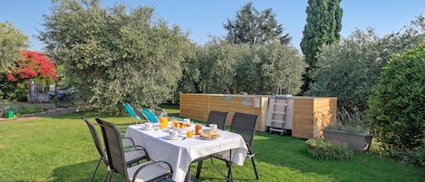 Un jardín con una mesa preparada para el desayuno, una estructura de madera y un árbol alto.