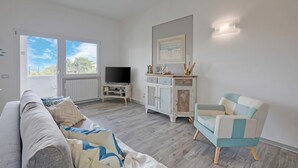 A living room with a sofa, a TV, a cabinet, and a chair. - Villa Ulivi private Pool & Lake View (San Felice del Benaco)