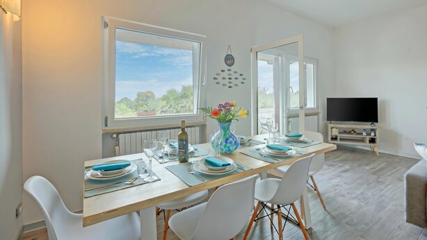 A dining area with a table set for four, a vase with flowers, and a television in the background. - Villa Ulivi private Pool & Lake View (San Felice del Benaco)