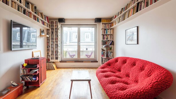 Een gezellige kamer met een rode relaxstoel, een klein tafeltje en een boekenplank vol boeken.