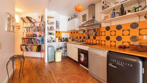 Een keuken met een koelkast, oven en diverse keukenspullen op planken.