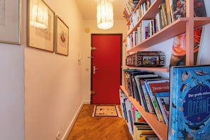 A hallway with a red door, framed pictures on the wall, and a bookshelf filled with books.