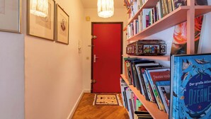 Een gang met een rode deur, ingelijste foto's aan de muur en een boekenplank vol boeken.